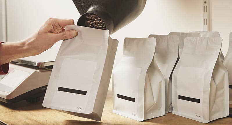 woman poring roasted coffee beans into white bags